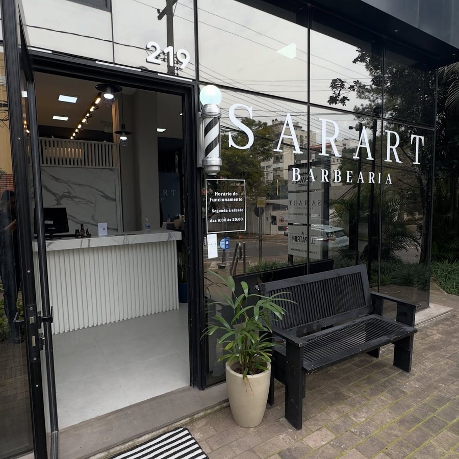 Fachada de vidro da unidade Petrópolis com Sarart Barbearia aplicado no vidro, número 219 e um banco na entrada.