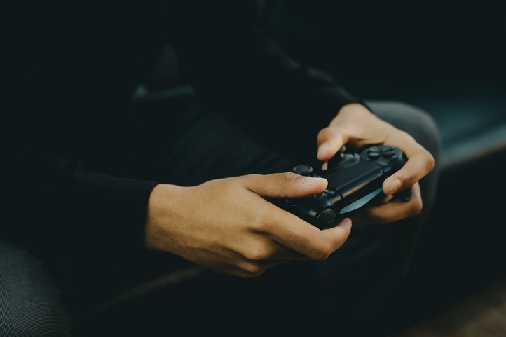 Mãos segurando um controle de videogame na penumbra da sala de espera.